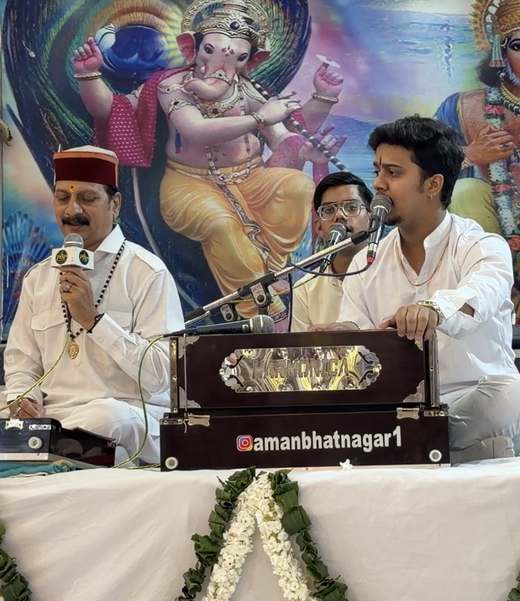 Prem Bhatnagar ji and two singers of the party in white kurtas singing bhajans at a prayer meeting, one playing the harmonium
