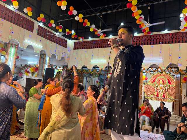 A singer of the party leading Shyam bhajans in a decorated temple hall as women dance and clap