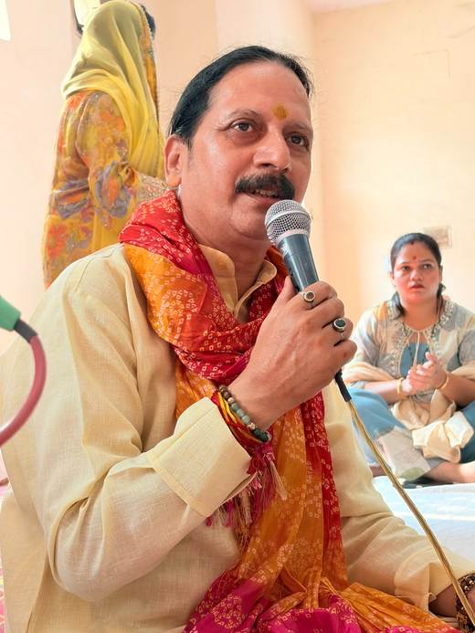 Prem Bhatnagar ji in a red and orange chunri singing bhajans as a devotee claps along