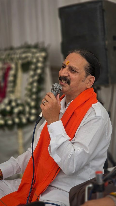 Prem Bhatnagar ji smiling as he speaks to the gathering, with the white flower frame behind him